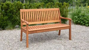 Eine Holzbank mit senkrechten Latten an Rückenlehne und Sitzfläche steht auf einer Kiesfläche, umgeben von grünen Sträuchern und Pflanzen. Genießen Sie stilvolle Gartenmomente mit diesem eleganten Stück von Casaria Gartenbänke, das für nur 95 Euro zu haben ist.