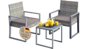 Zwei graue Casaria Polyrattan Gartenmöbel-Stühle mit Kissen und ein passender quadratischer Tisch mit einem Krug Orangensaft, Gläsern und Orangenscheiben. Ein Schild mit der Aufschrift „Robust & Stabil“ und einer deutschen Flagge – perfekt für Ihr Lounge-Set.